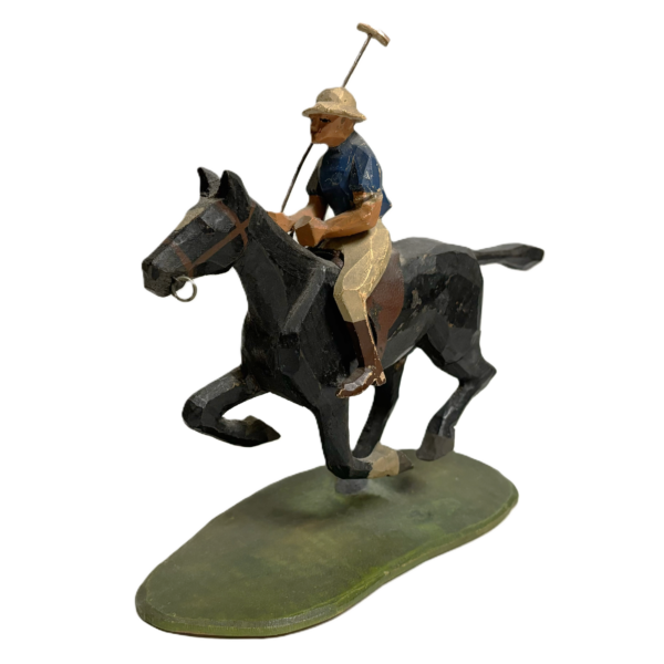 A hand carved wooden sculpture of a polo player who holds is mallet and is mounted on a black horse.