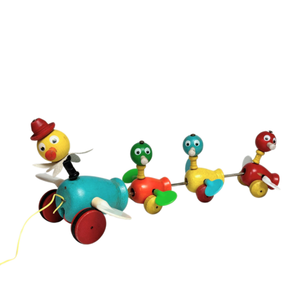 A classic toy, the Fisher Price wooden 'Ducks in a Row' pull toy, is a vibrant and playful piece. Crafted from wood, it features one large duck followed by three small ducks, all painted in multiple bright colors. The ducks are simple shapes with cute features, and as you pull the toy, the plastic wings spin.